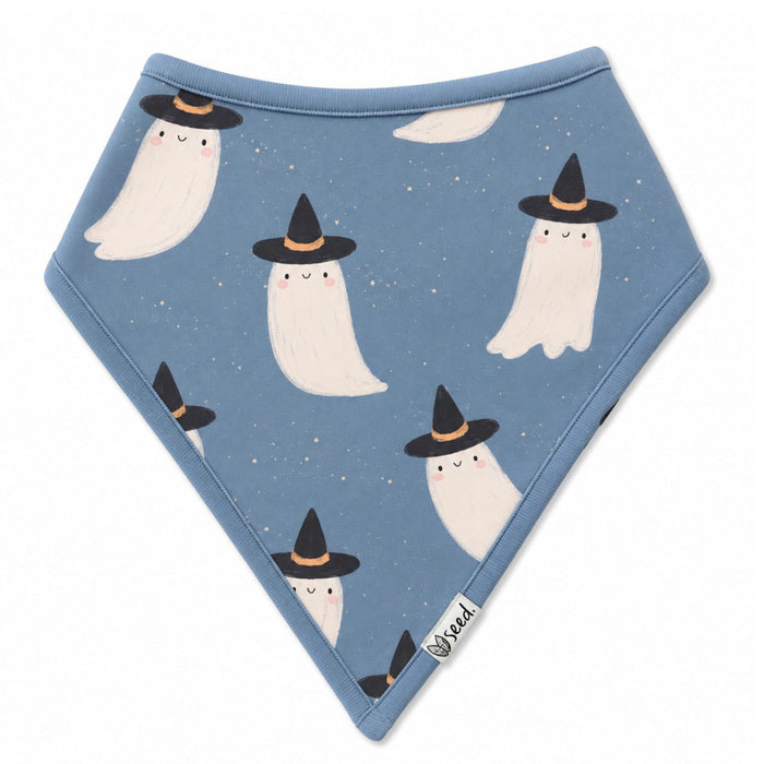 A triangular baby bandana bib in dusty blue, featuring a repeating pattern of cute white ghosts wearing black witch hats. The bib is laid flat on a clean white background, with a small white brand tag near the bottom right corner.