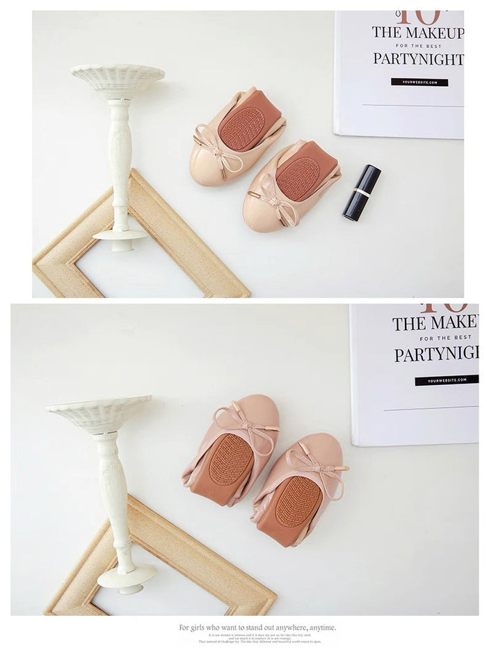Pair of pink baby shoes with a bow on a white surface with a magazine in the background.