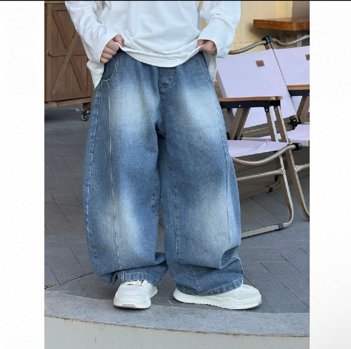Person wearing oversized blue jeans and white sneakers on a wooden floor.