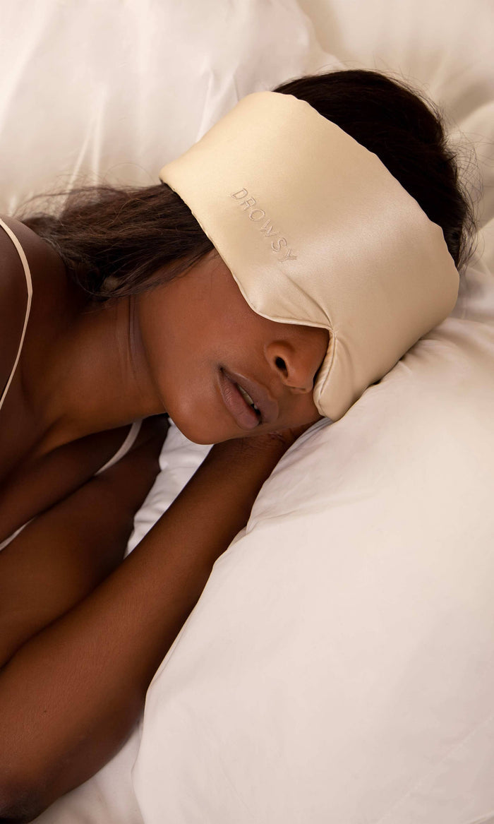 Person wearing a cream-colored sleep mask in bed