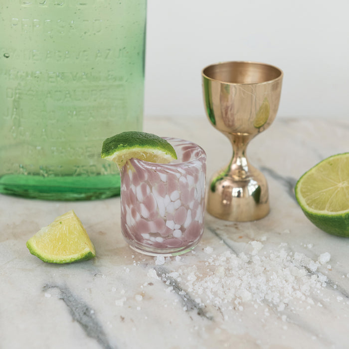 Cocktail setup with a pink glass, gold shaker, and lime wedges on a marble surface.