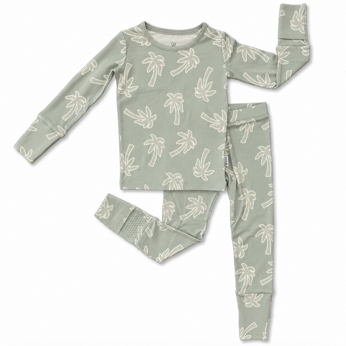 A two-piece children's pajama set featuring a long-sleeve top and matching pants in a muted sage green color, both printed with a white palm tree pattern. The set is laid flat on a clean white background.
