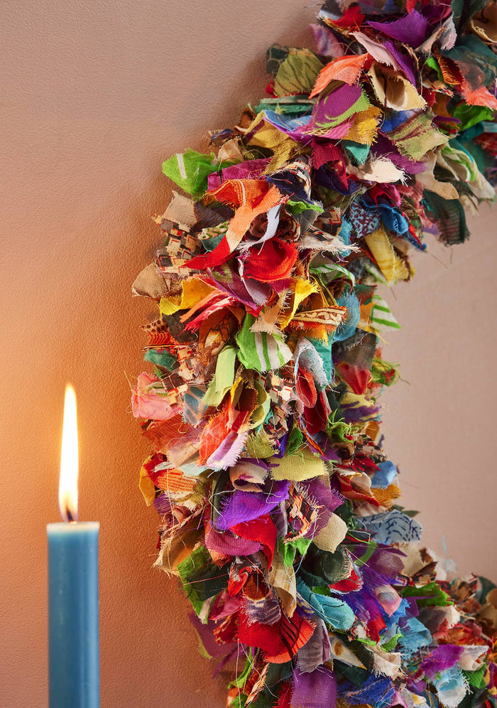 Colorful fabric wreath with a lit candle on a plain background