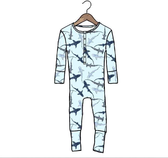 A children's long-sleeve one-piece pajama or henley jumpsuit hanging on a wooden hanger against a plain white background. The garment has an allover shark print in dark blue and gray on a very light icy blue base.