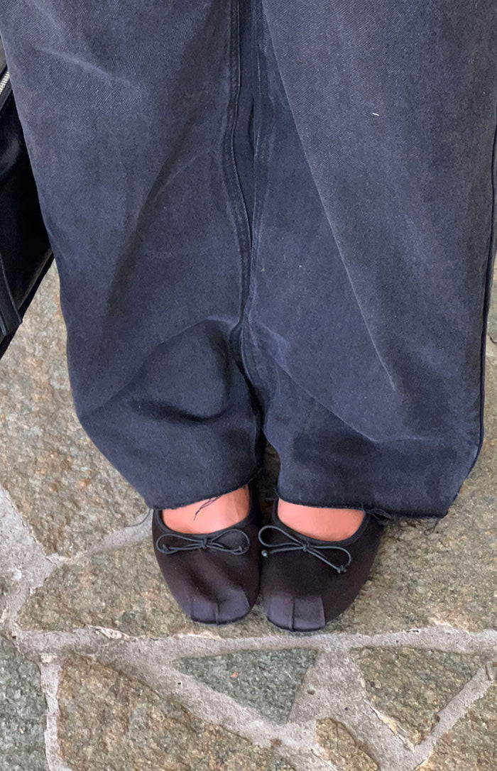 Top-down view of black satin ballet flats featuring small decorative bows on the rounded toes