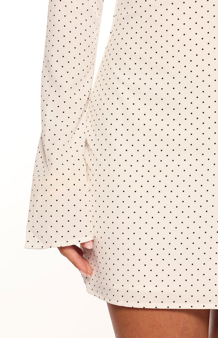 Close-up of the cream polka dot mini dress showing the flared long sleeve cuff and skirt hem