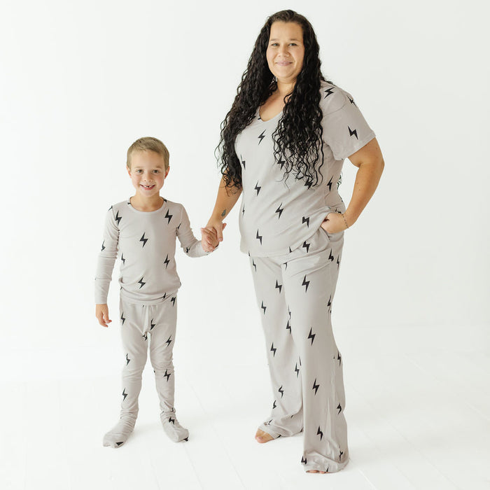 A woman and a young boy wearing matching light gray pajama sets with a black lightning bolt pattern, standing and holding hands against a plain white studio background.