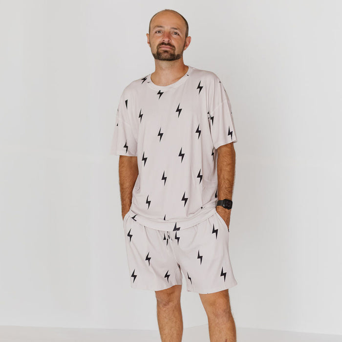 A man wearing a matching light beige lounge set with a black lightning-bolt pattern, consisting of a short-sleeve t-shirt and drawstring shorts, standing against a plain white studio background.