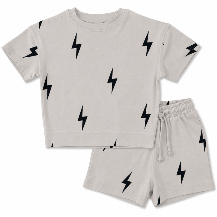 A two-piece kids' loungewear set featuring a short-sleeve t-shirt and matching shorts in a light beige or oatmeal color, both printed with a black lightning bolt pattern. The set is displayed flat against a solid white background.