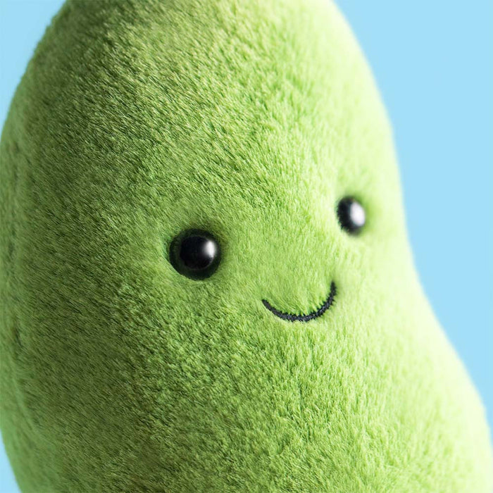 Jellycat Amuseables Soyella Edamame Bean — close-up of the plush green edamame bean's face showing black hard eyes and an embroidered smile, on a light blue background