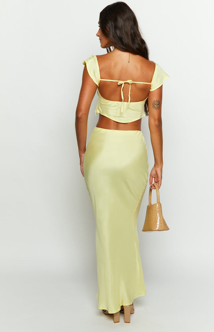 Rear view of a yellow satin maxi skirt, fitted through the hips and flowing to a slight flare at the hem
