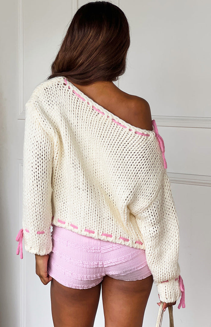 Rear view of a cream chunky knit sweater with an off-shoulder neckline and pink contrast stitching and ties