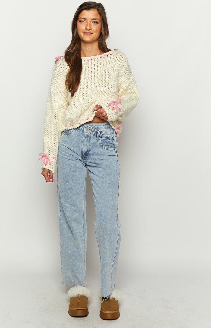 Cropped cream chunky knit sweater with pink lacing detail along the hem and boat neck, pink ribbon bows on sleeves