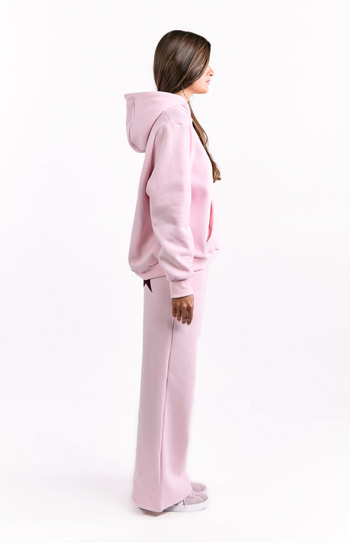 Side view of an oversized light pink hoodie and matching wide-leg pants with a burgundy star detail