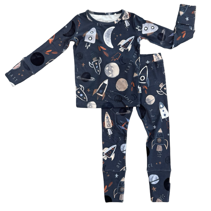 A two-piece children's pajama set featuring a long-sleeve top and matching pants in dark navy blue with a playful outer-space print of rockets, moons, planets, and stars.