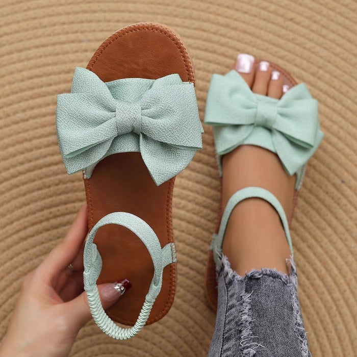 Mint green sandals with large bows worn by a person on a textured brown background