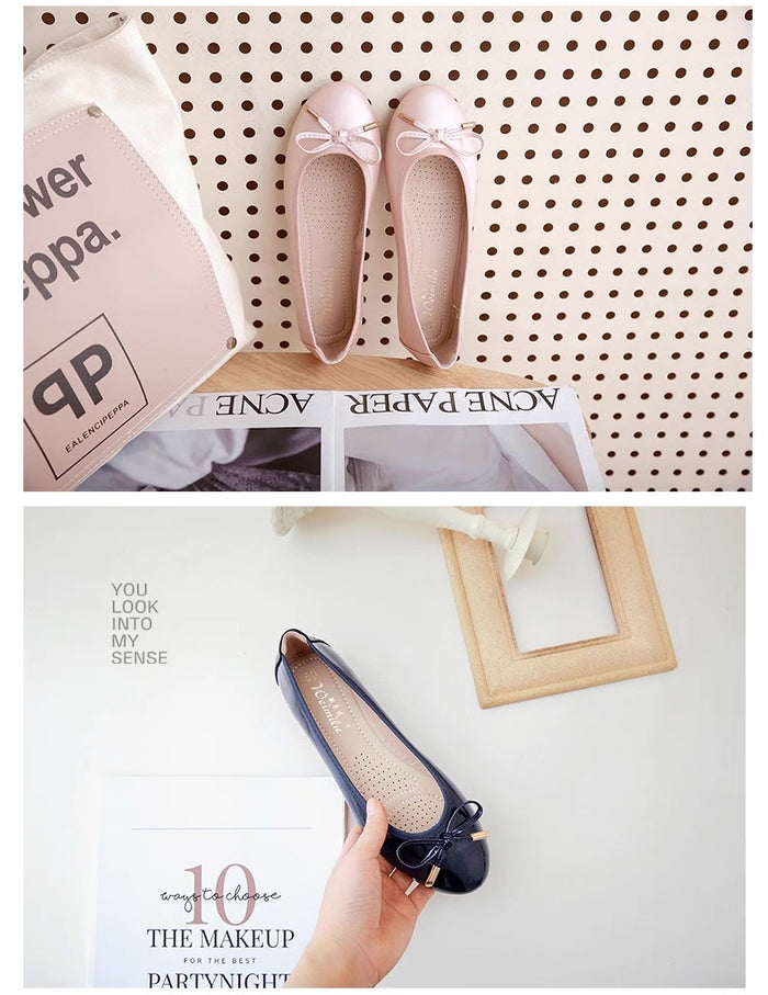Pair of pink flats with a bow on a white background, held by a hand.