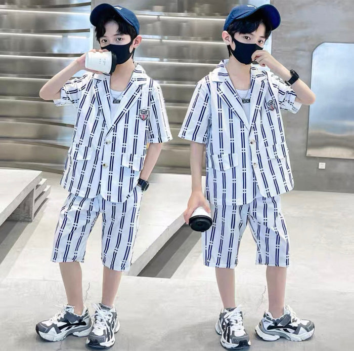 Two children wearing matching outfits with plaid shirts and shorts, standing indoors.