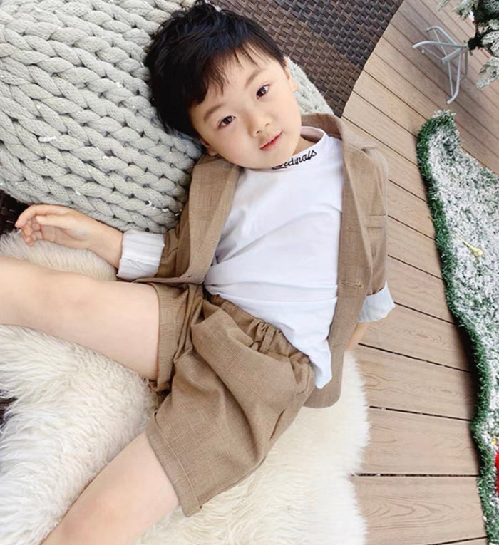 Child wearing a beige outfit with suspenders lying on a textured surface