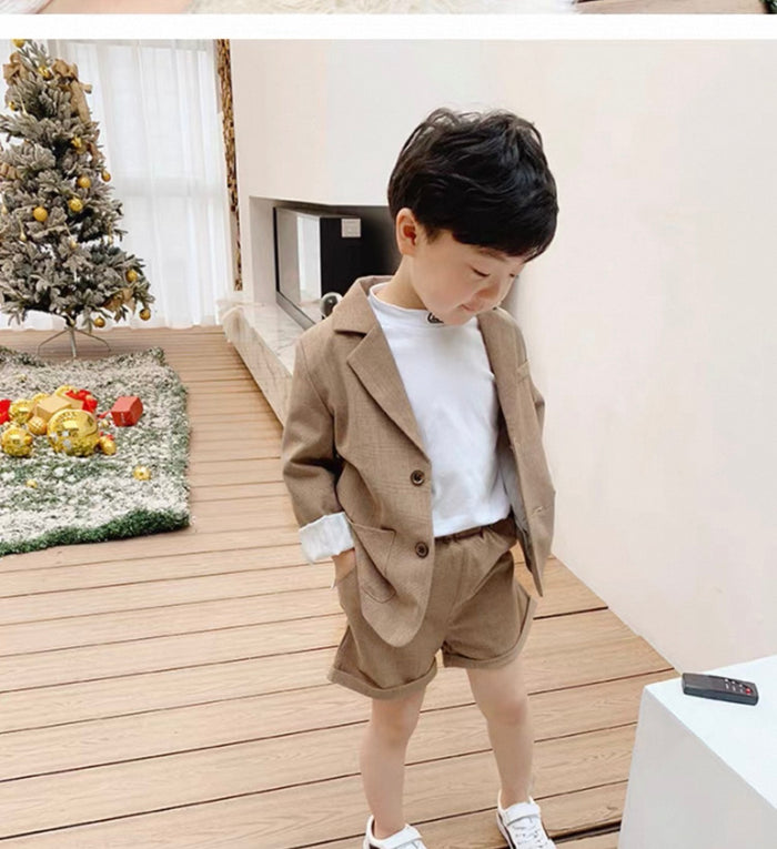 Child wearing a beige suit standing in a room with a Christmas tree in the background