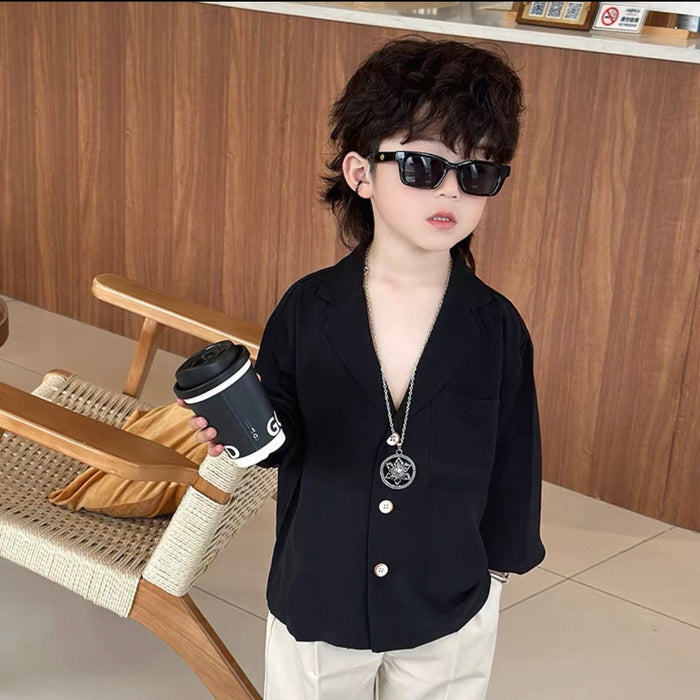 Child wearing sunglasses and a black blazer holding a coffee cup indoors.