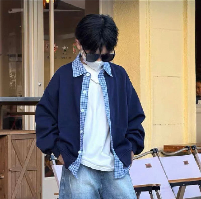 Person wearing a navy cardigan, plaid shirt, and jeans standing outdoors.