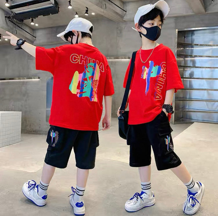 Two children wearing red t-shirts with colorful designs, standing in a modern indoor setting.