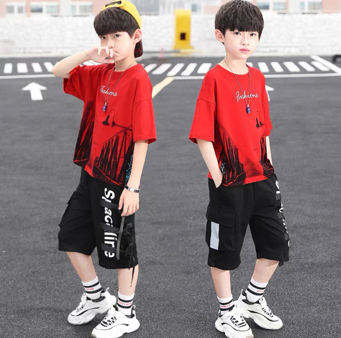 Two children wearing matching red t-shirts and black shorts on a street.