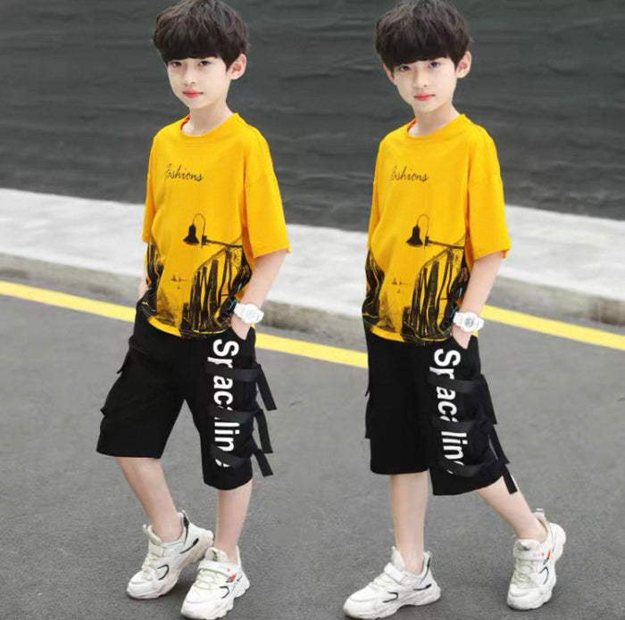 Two children wearing matching yellow t-shirts and black shorts with white text, standing on a road.