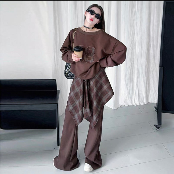 Person wearing a brown outfit with a plaid scarf, holding a coffee cup, in a minimalistic room.