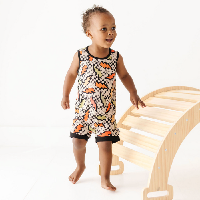 Child in a patterned outfit standing next to a wooden climbing toy on a white background
