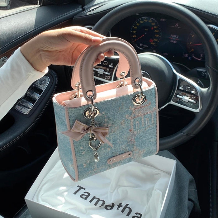 Small handbag held in front of a car dashboard with 'Tamatha' branding.