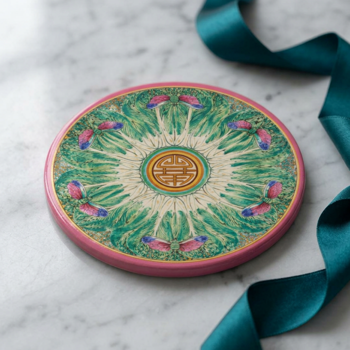 Round sandstone coaster with a pink border, green bok choy-inspired pattern, and dragonfly details on a marble surface.