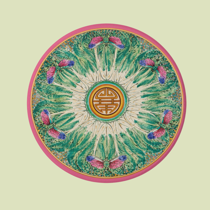 Round sandstone coaster with a pink border, green bok choy-inspired pattern, and dragonfly details on a marble surface.