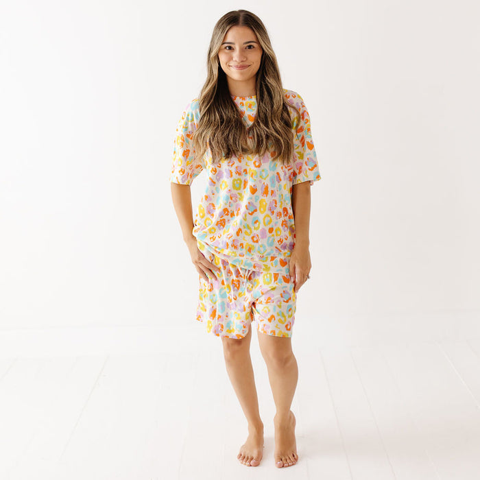 A woman modeling a matching short-sleeve pajama top and shorts set with a colorful retro pattern on a white background.