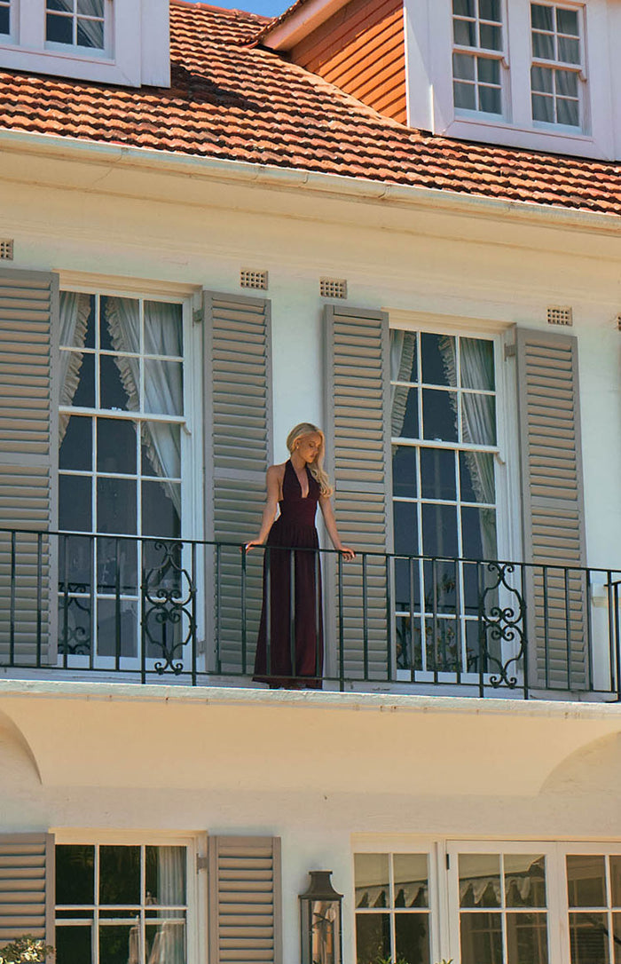 Full length view of a burgundy halter neck maxi dress with a deep V-neckline and flowy skirt