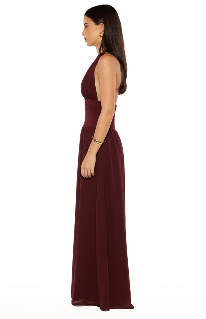 Side view of the burgundy halter neck maxi dress with a fitted ruched waist and flowing skirt