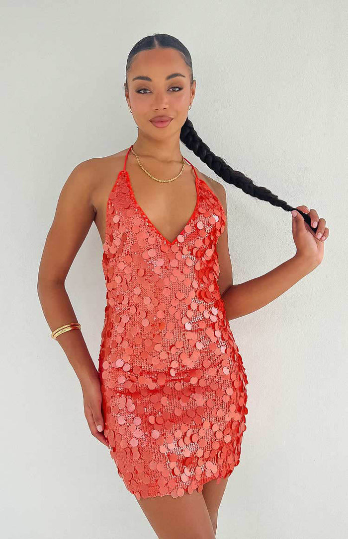Close-up of the orange sequin mini dress showing the deep V-neck halter neckline and fitted silhouette