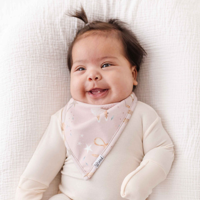 Baby wearing a pink bib with a smile on a white blanket