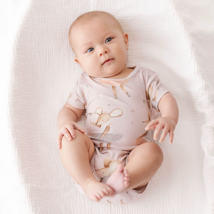 Baby lying on a white blanket wearing a light pink onesie with animal prints.