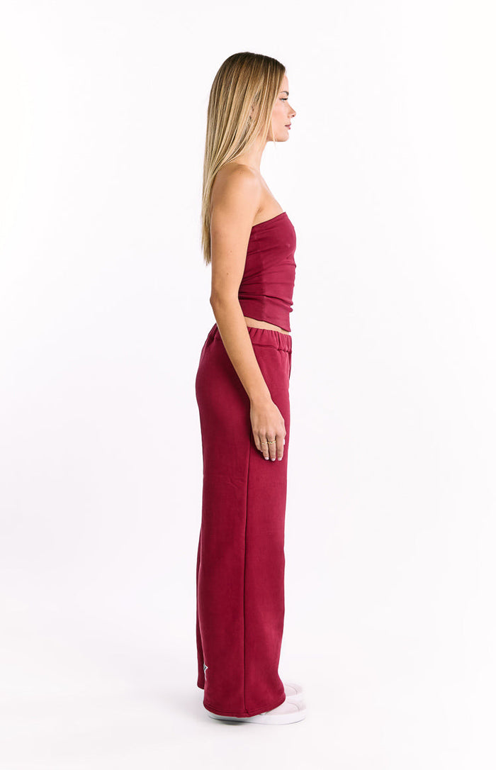 Side view of burgundy wide-leg track pants with an elasticated waistband and small star logo near the hem