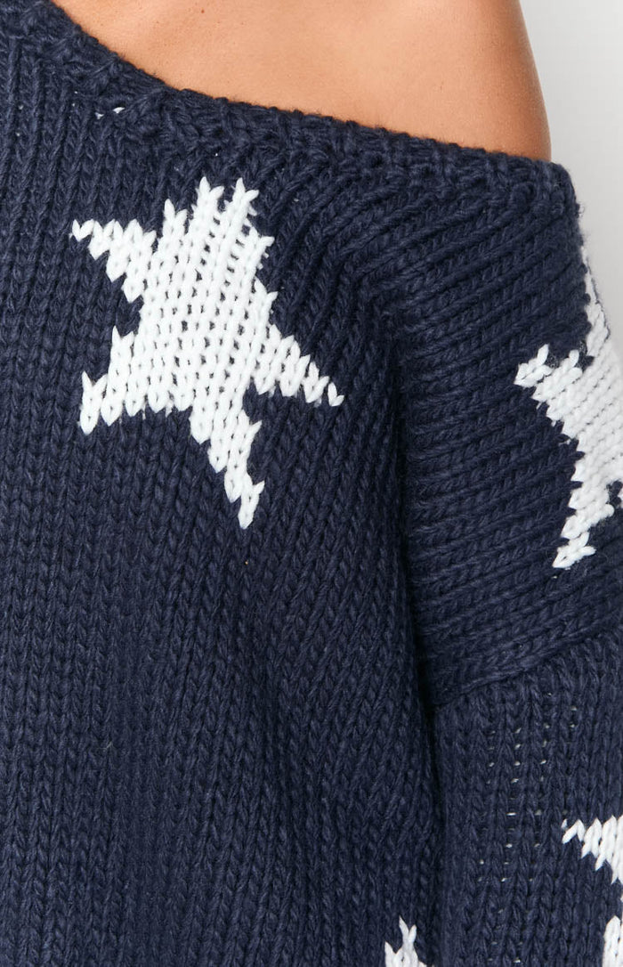 Close-up of the navy chunky knit sweater showing the white star pattern and off-shoulder neckline