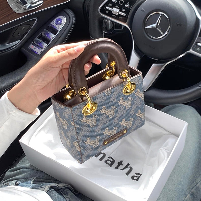 Hand holding a patterned handbag with gold accents in a car interior.