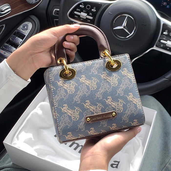 Hand holding a patterned handbag with gold accents in a car interior.