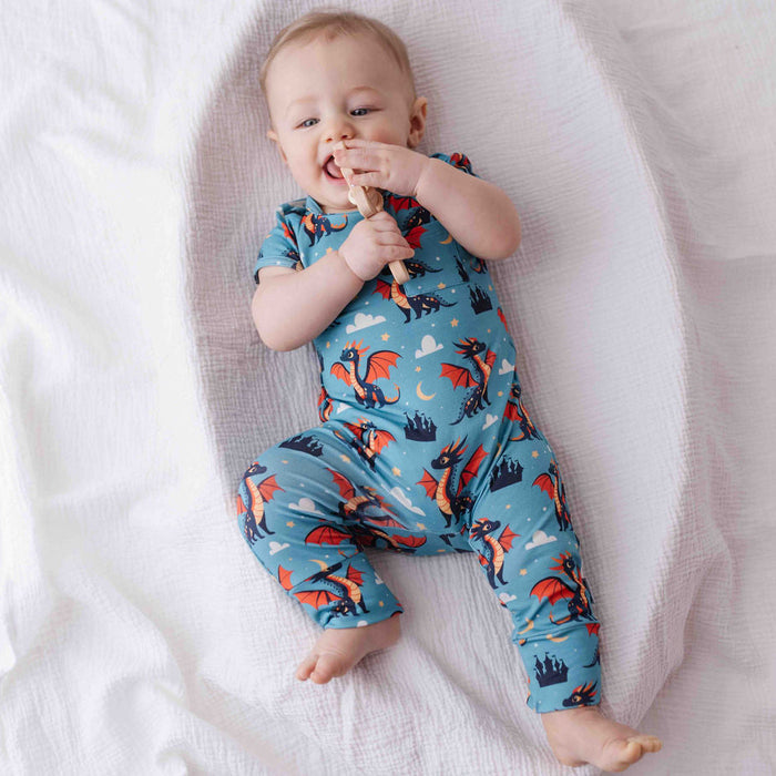 Baby wearing a blue romper with dragon print on a white blanket