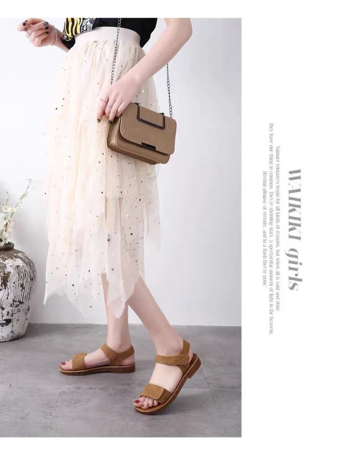 Person wearing brown sandals and holding a matching handbag, standing against a plain background.