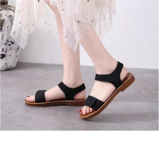 Black sandals with brown soles worn by a person on a light gray floor.