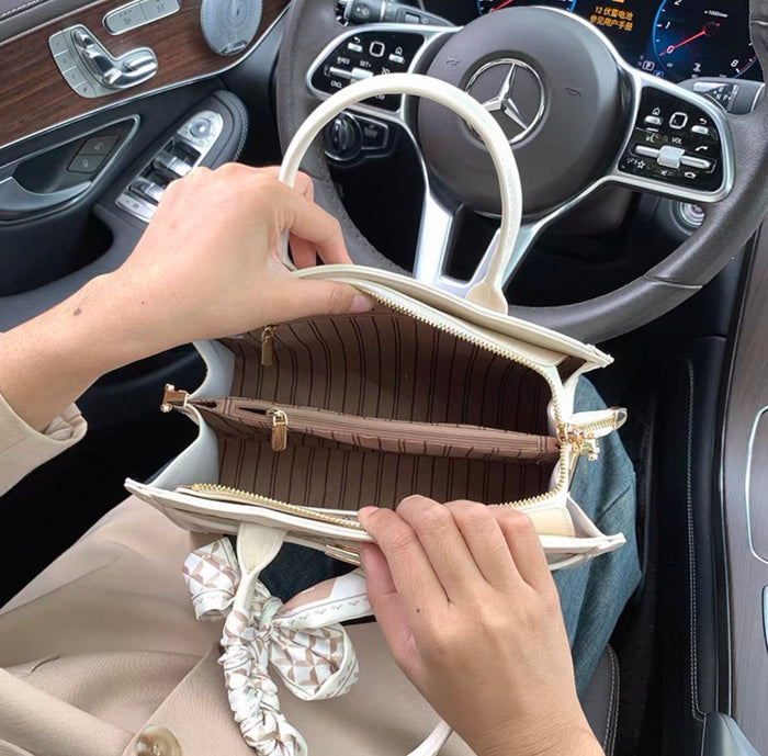 Cream-colored structured leather handbag with top handle and gold hardware, striped brown fabric interior lining, and zipper