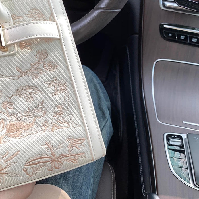 Cream leather Kelly-style handbag with intricate floral and bee embroidery and top handle.