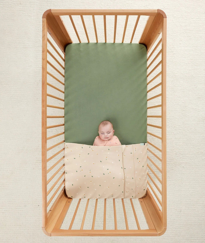 Baby sleeping in a wooden crib with HugMe Blanket from Ergopouch, perfect for bare mum postpartum